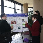 Students give brief overview of poster presentation to interested audience
